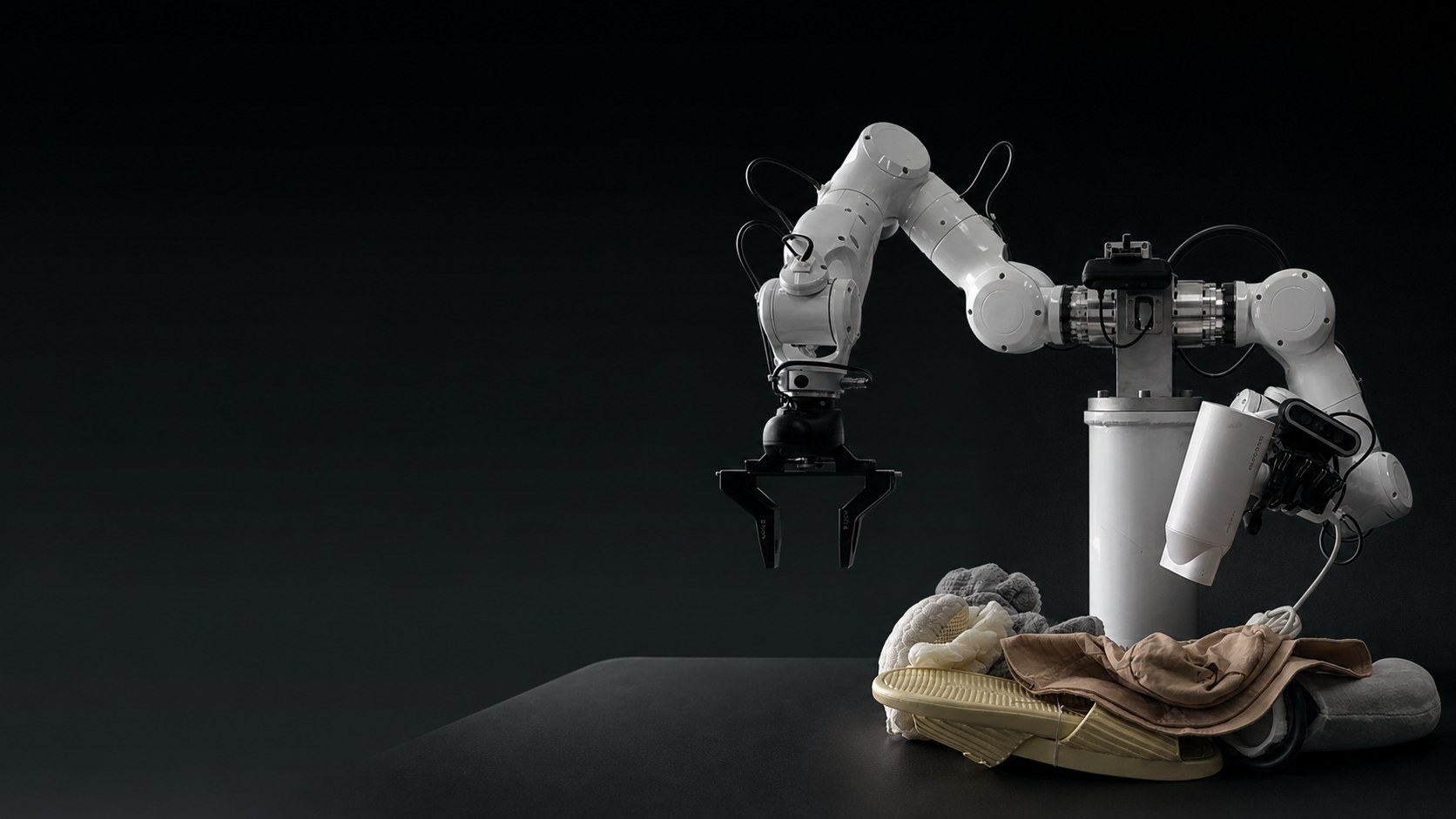 White dual-arm robot with a black two-finger gripper over a pile of clothes and a yellow slipper