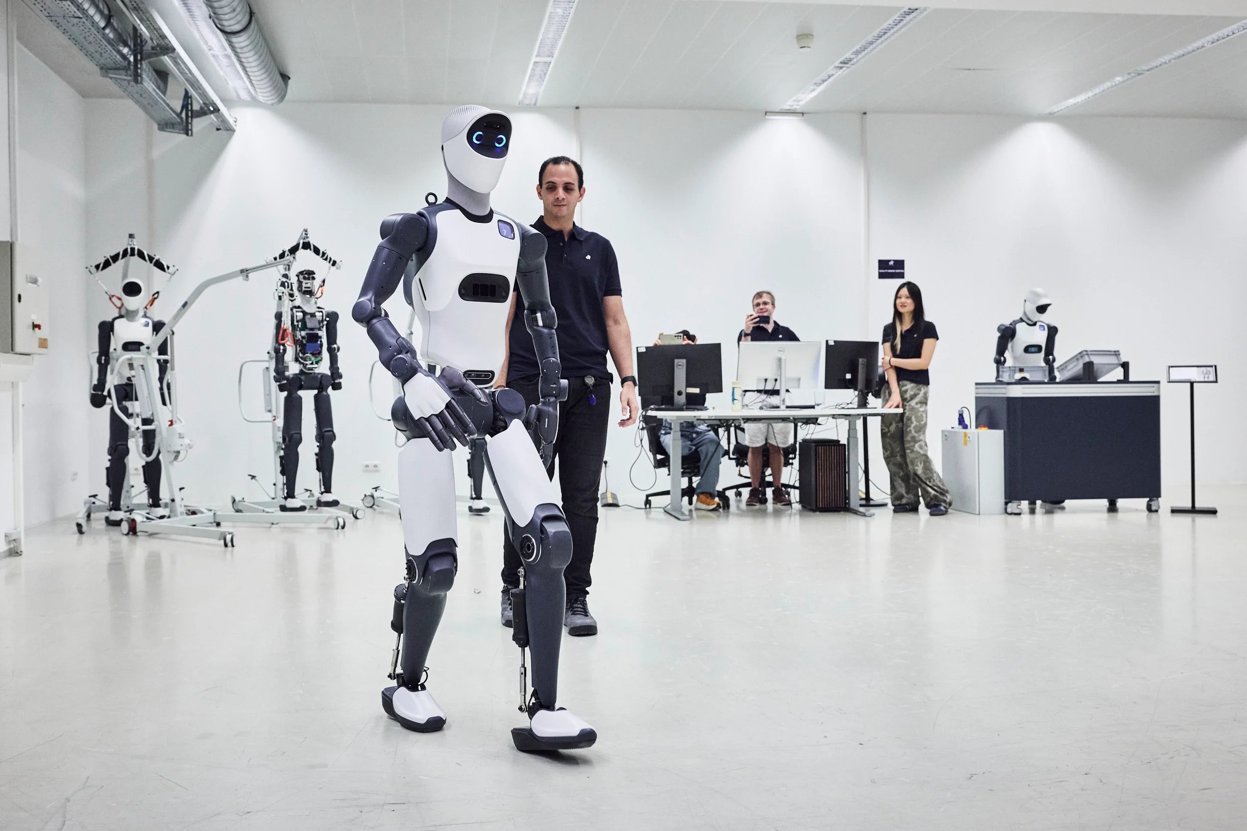 Agile ONE walking untethered in a white lab with an engineer following and other units in the background
