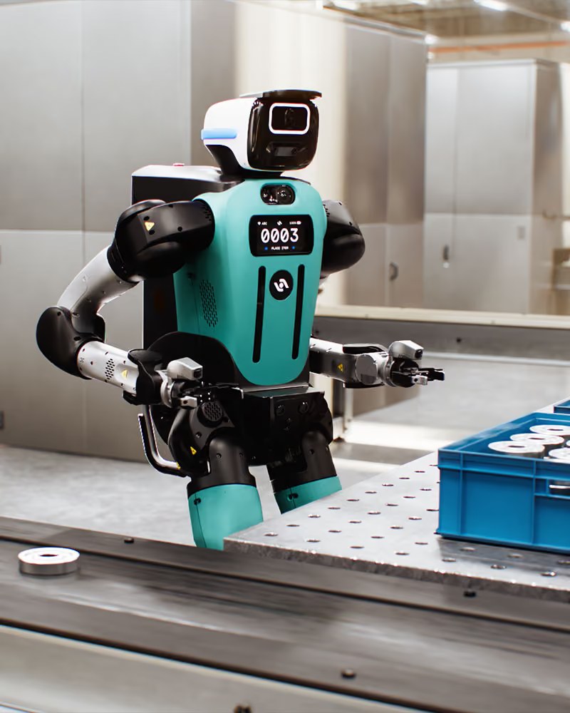 Digit 5 standing at a factory workbench with a blue crate of circular parts