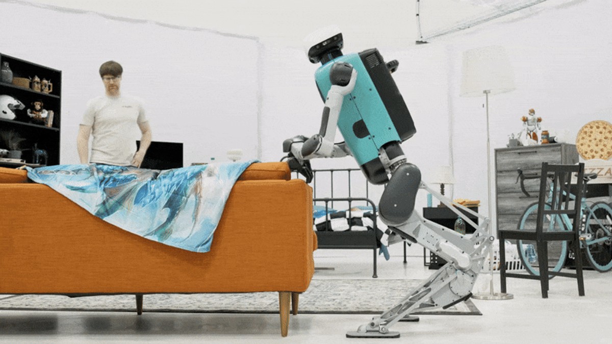 Digit gripping and dragging an orange sofa in a staged living room