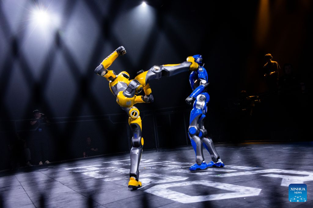 Yellow EngineAI T800 kicking a blue T800 in a Riyadh combat arena