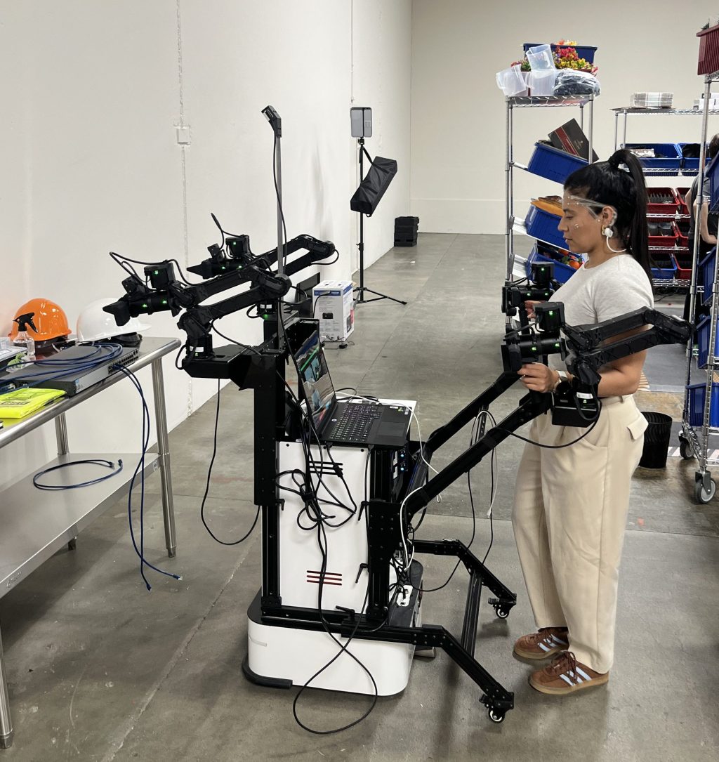 Robot pilot Sofia Infante operating a leader-follower dual-arm rig in Encord’s warehouse