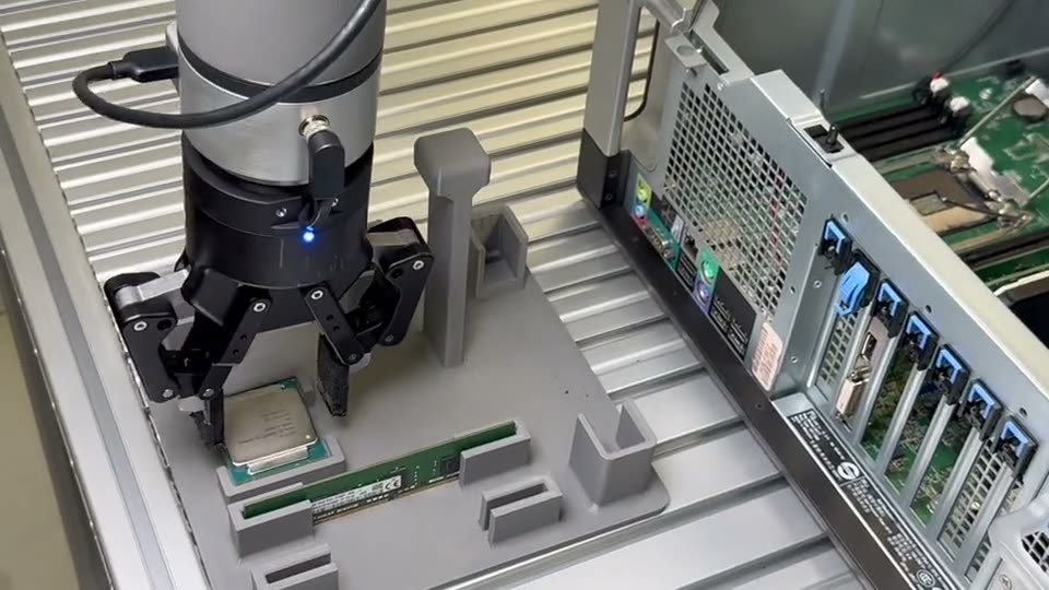 Parallel gripper holding a CPU over a fixture next to an open PC chassis