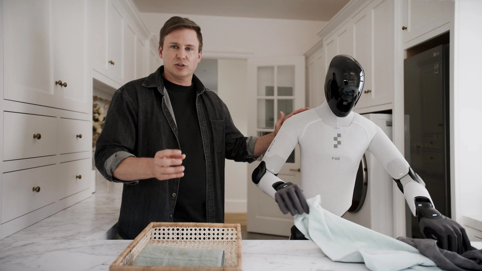 Brett Adcock standing beside Figure 03 folding a towel on a kitchen island