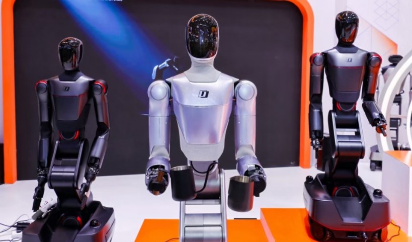 Three Galaxea wheeled dual-arm robots on a WRC booth, the center unit holding two cups