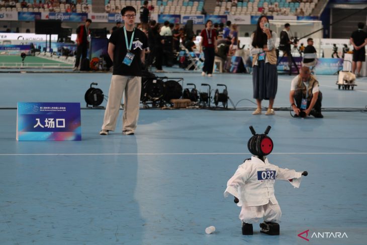 Tiny humanoid bib 032 in a white martial-arts uniform on the blue court