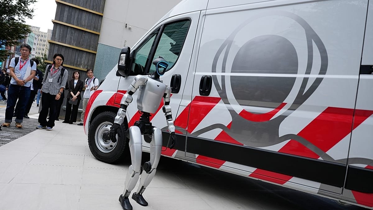 A silver humanoid standing beside GMO’s red-striped maintenance van