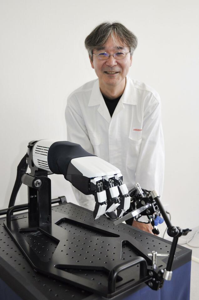 Honda R&D engineer Takahide Yoshiike standing behind the multi-fingered hand on a lab table