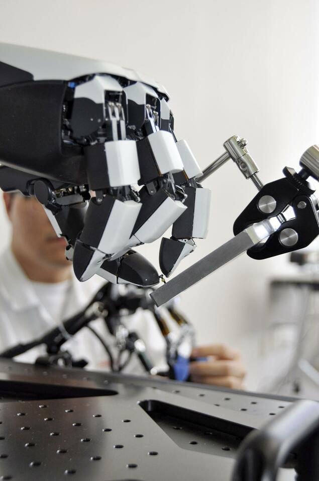 Close-up of Honda’s four-finger hand gripping a small metal bar in a lab fixture