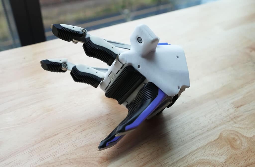 Motorized Koala robot gripper on a wooden table, two fingers and a dual thumb visible