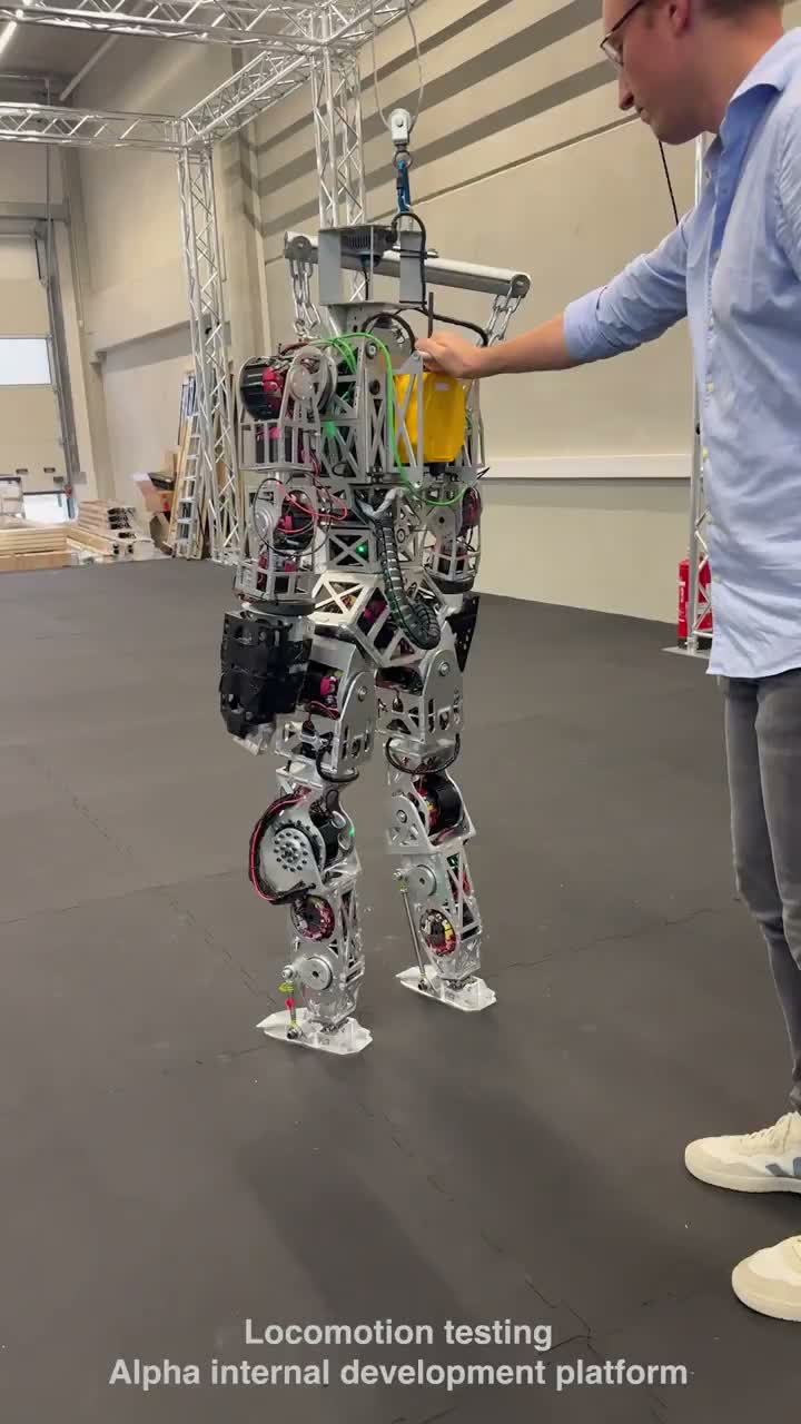 Person in a blue shirt standing beside the walking Kyle prototype on a black floor