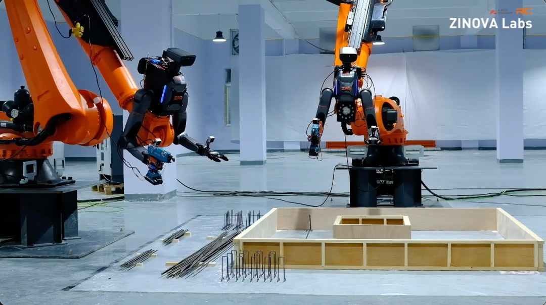 Two TRON 2 torsos on orange booms over a wooden formwork box with rebar laid out on the floor