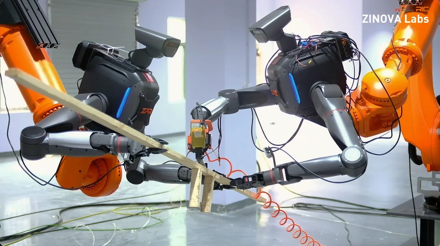 Two TRON 2 dual-arm torsos on orange industrial arms holding a wooden board while one drives a pneumatic nail gun
