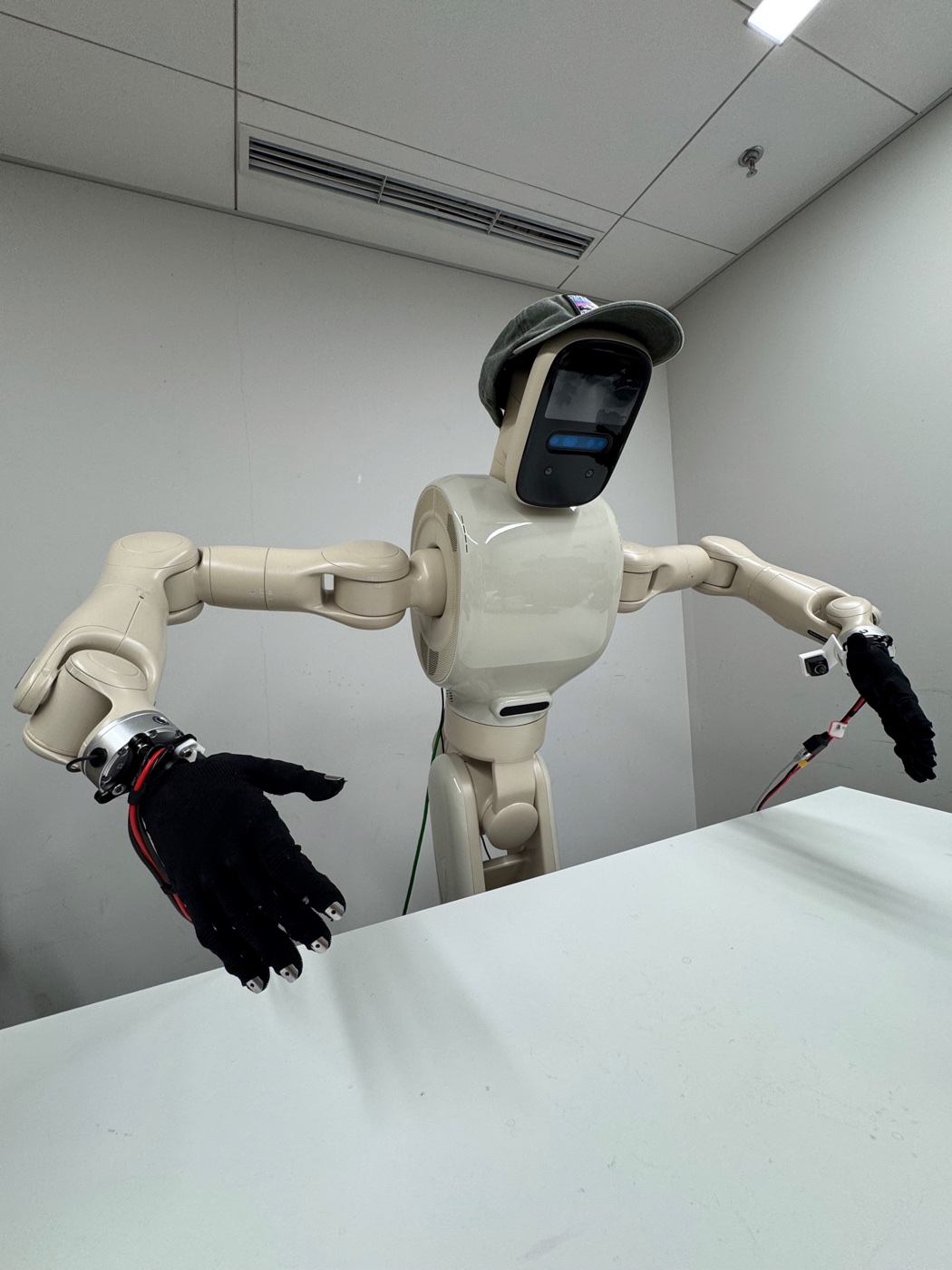 Beige dual-arm robot wearing a cap and Wuji Hand 2 gloves at a white table