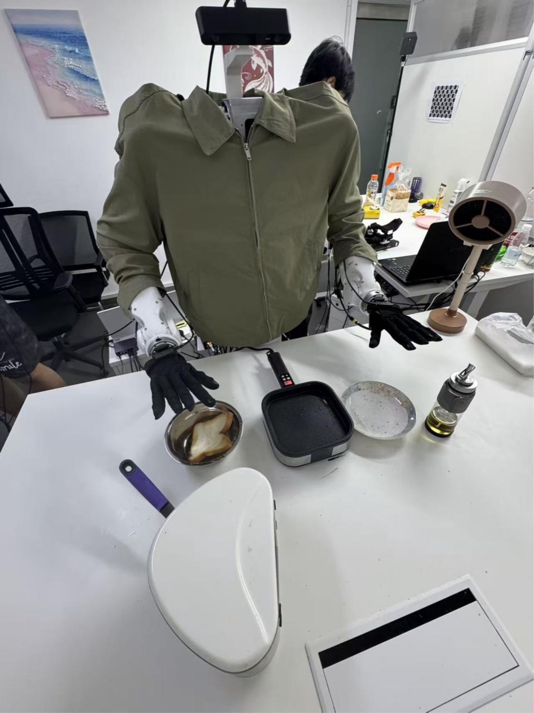 Headless dual-arm torso in a green jacket with black Wuji hands over a pan of toast