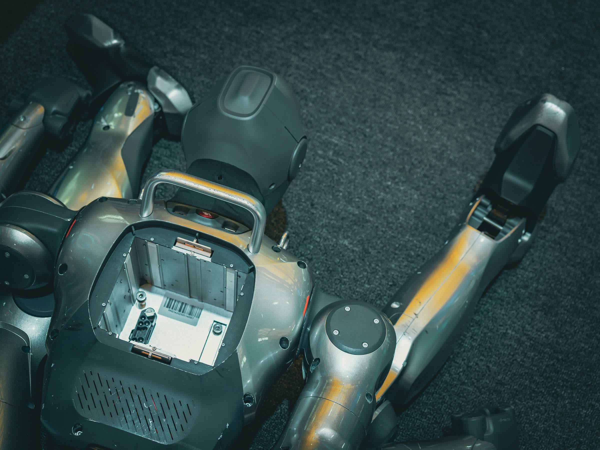 Overhead view of a metallic humanoid robot on the floor with open torso compartment