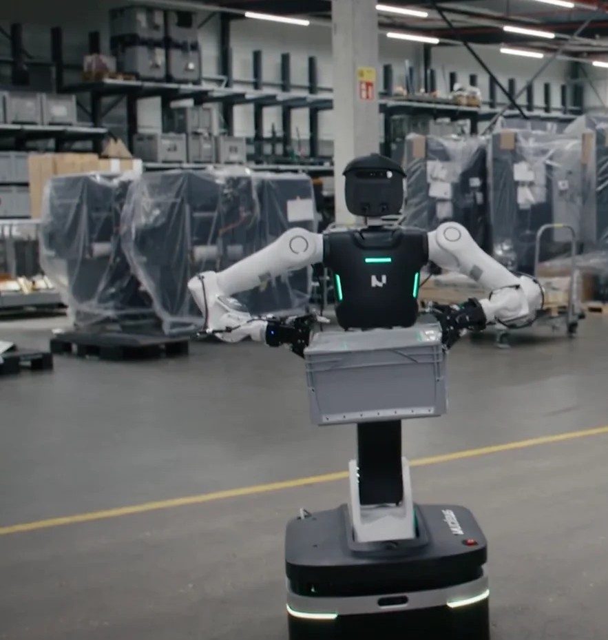 Nucleus II wheeled dual-arm holding a gray logistics bin in a warehouse aisle