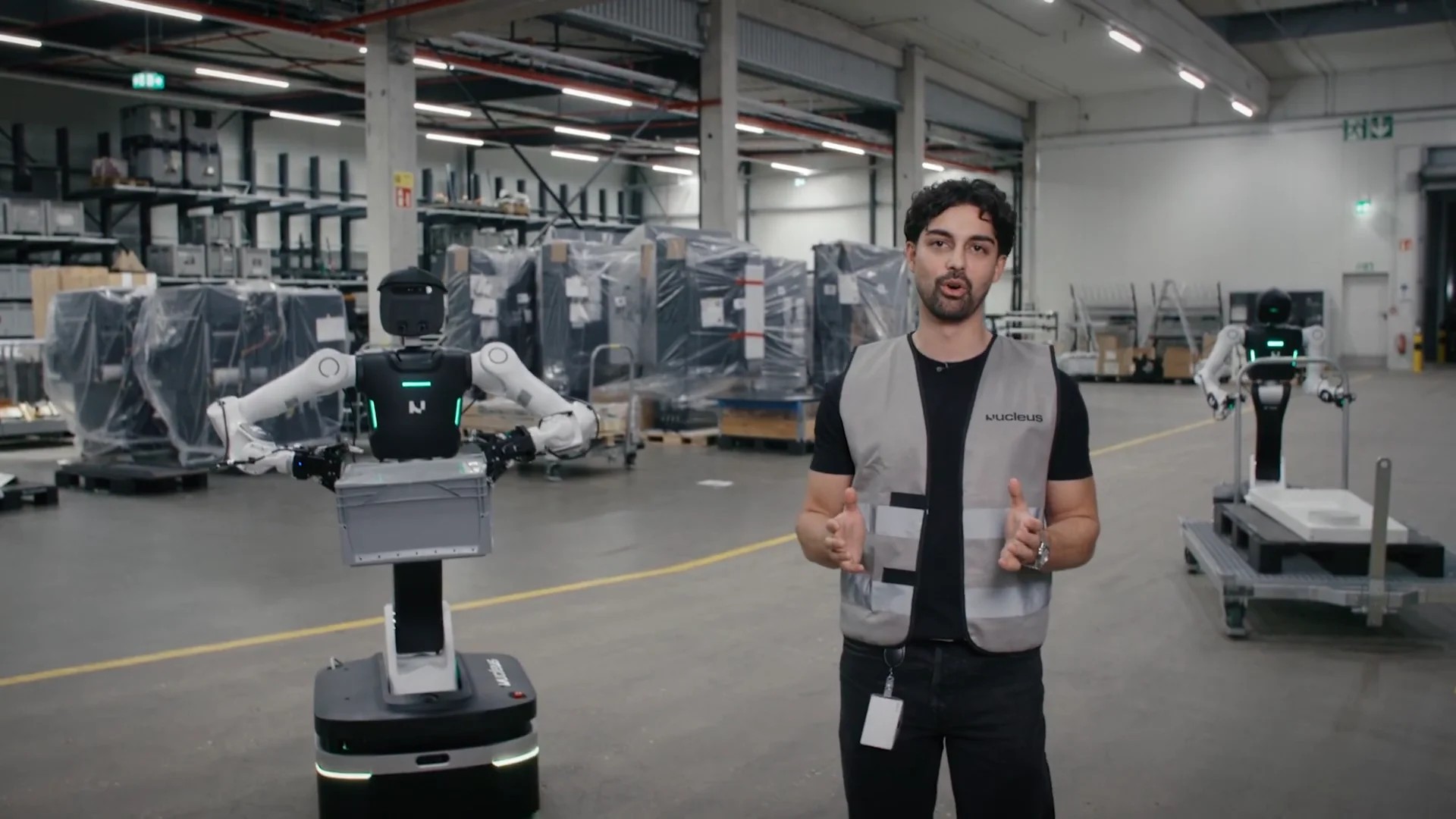 Melvin Schwarz standing in a warehouse next to a wheeled Nucleus II robot holding a gray tote