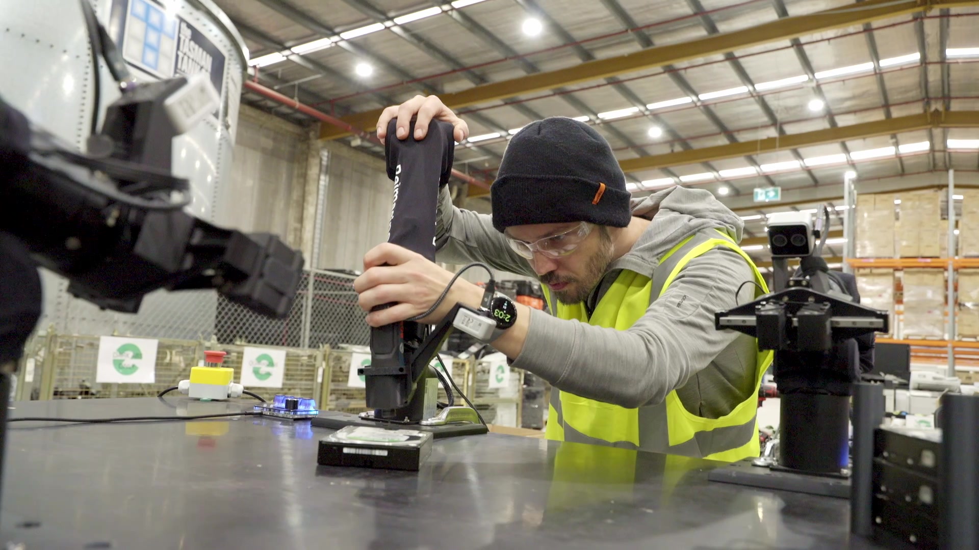Worker guiding a robot arm over a hard drive on a workbench