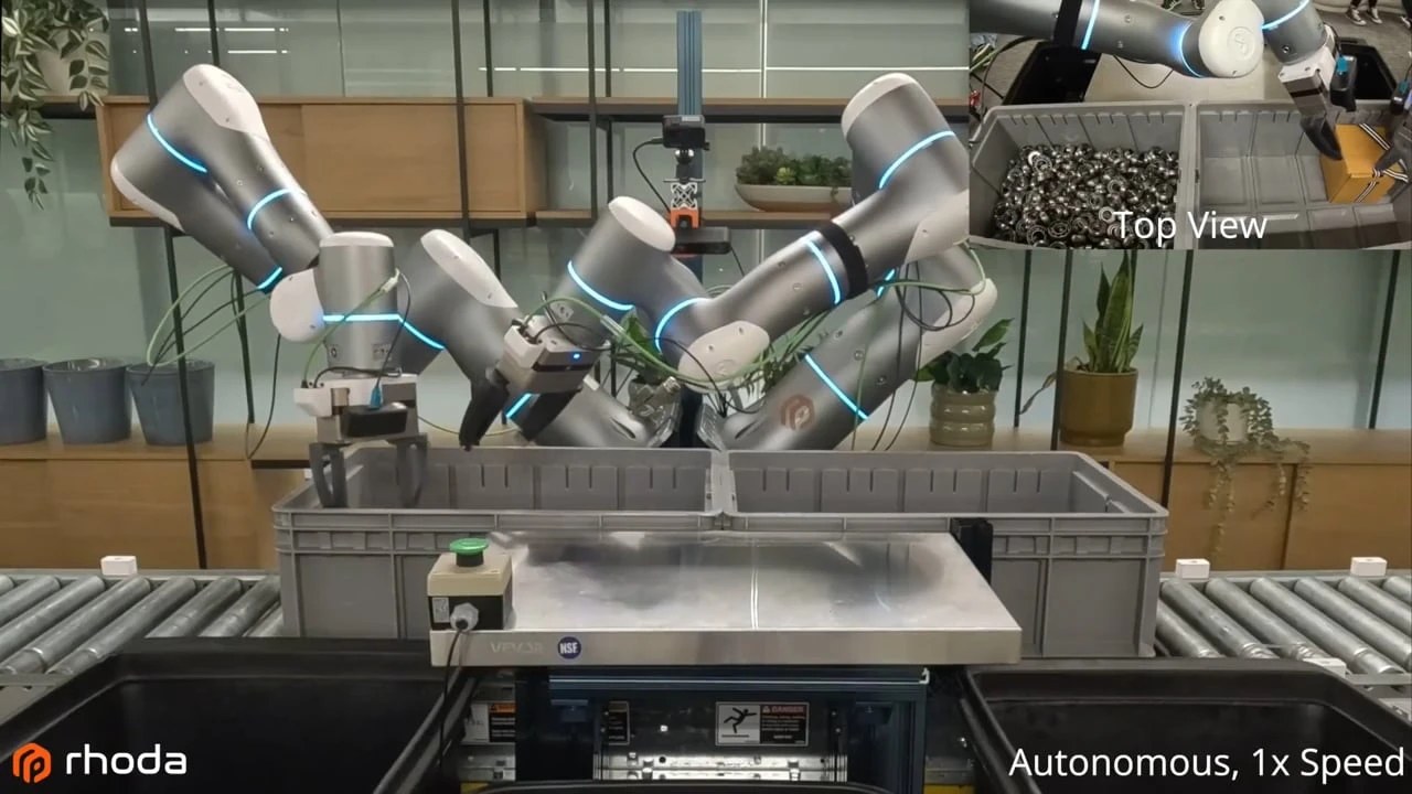 Two gray robot arms with blue rings unpacking bearings from gray totes on a conveyor