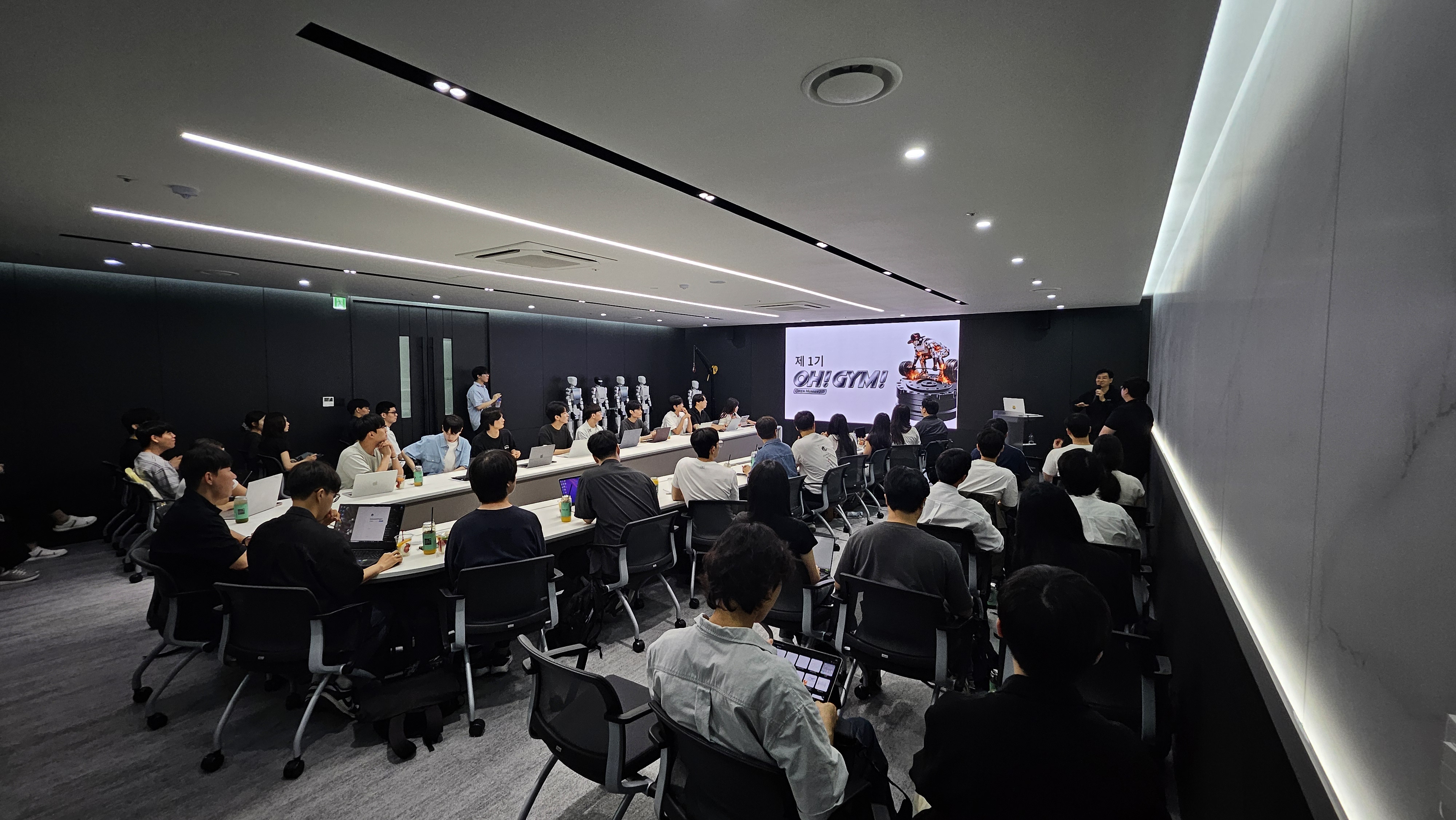 Lecture room with OH! GYM! on the screen and a row of white humanoids along the back wall