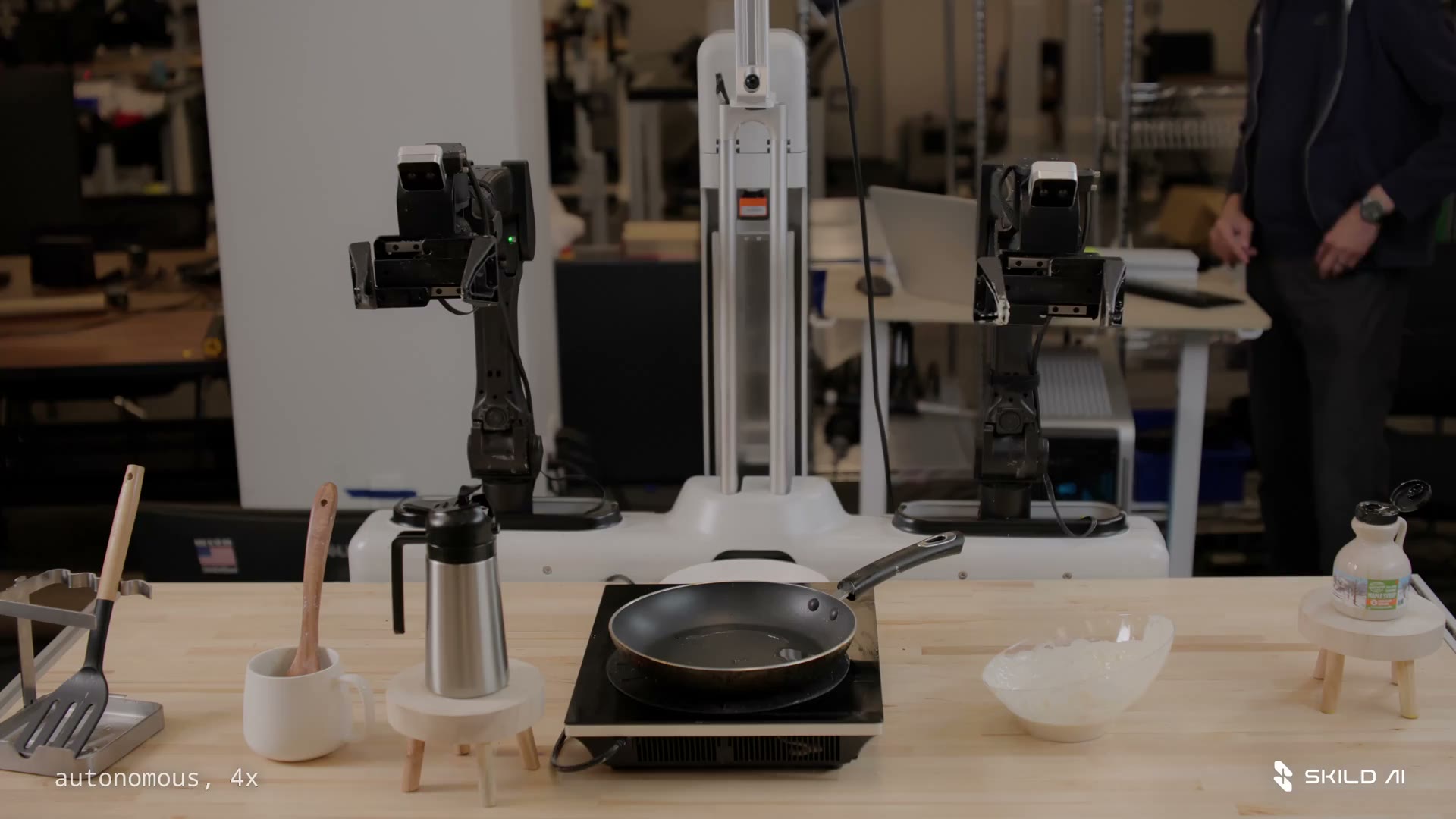 Dual robot arms at a skillet and hot plate labeled autonomous 4x, Skild AI logo