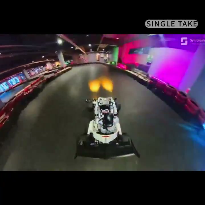 Overhead view of a humanoid seated in a go-kart on an indoor track, labeled single take