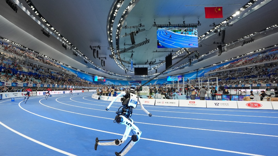 White humanoid with bib 001 sprinting on a blue indoor track with high, stiff arm swing
