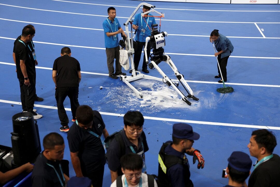 A fallen humanoid on a blue track being lifted by a hoist while staff mop foam