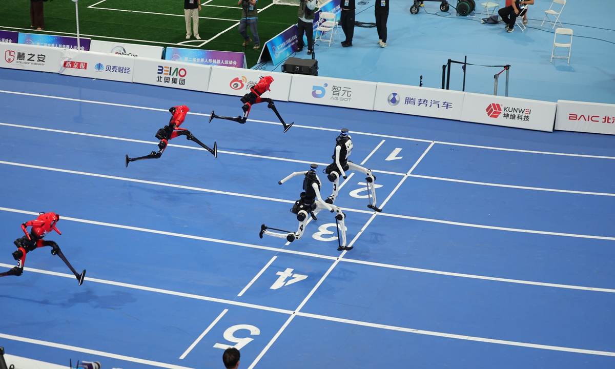 White and red humanoid robots sprinting on a blue indoor track at the World Humanoid Robot Games