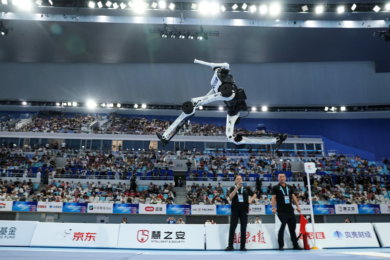 A white-and-black humanoid robot in mid-air during the long jump at Beijing’s National Speed Skating Oval