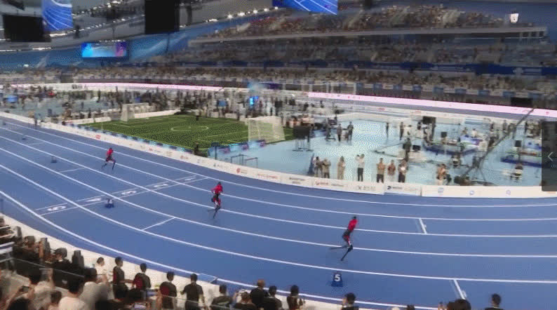 Wide view of humanoids running on the indoor oval with a soccer pitch in the infield