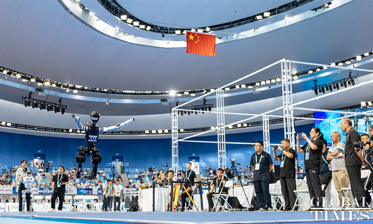 A white-and-black humanoid robot airborne with arms out over a blue indoor floor