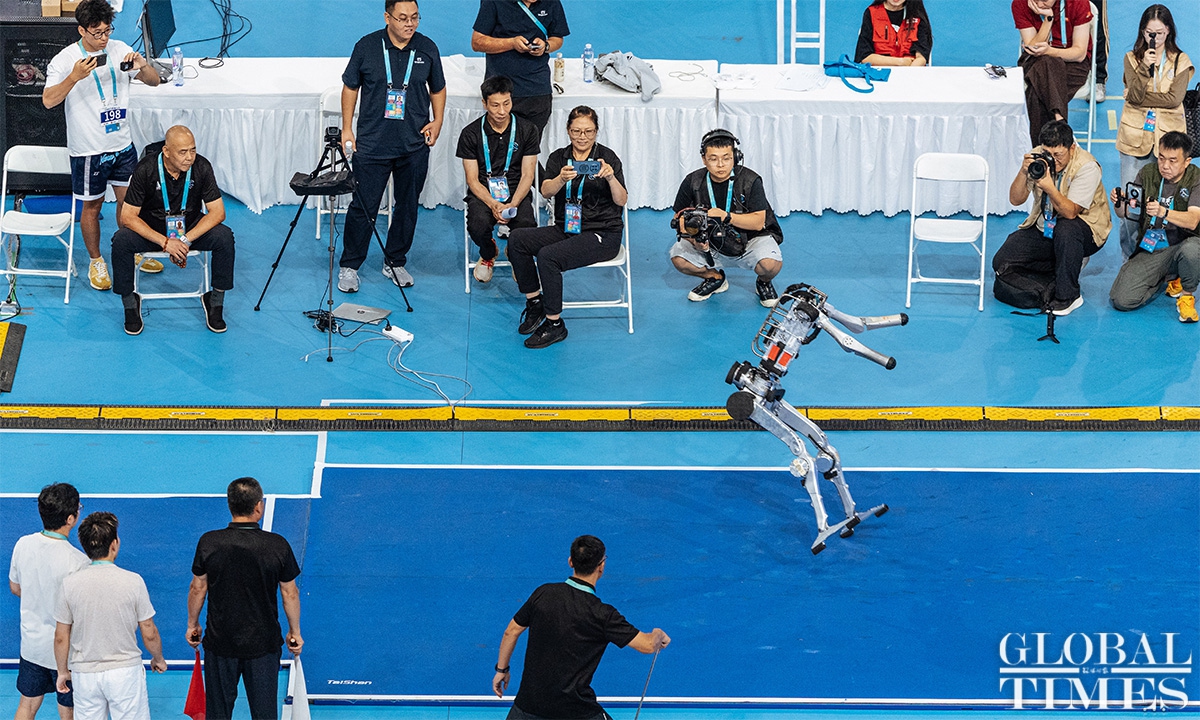 A humanoid robot on the jump board as an official with a red flag watches