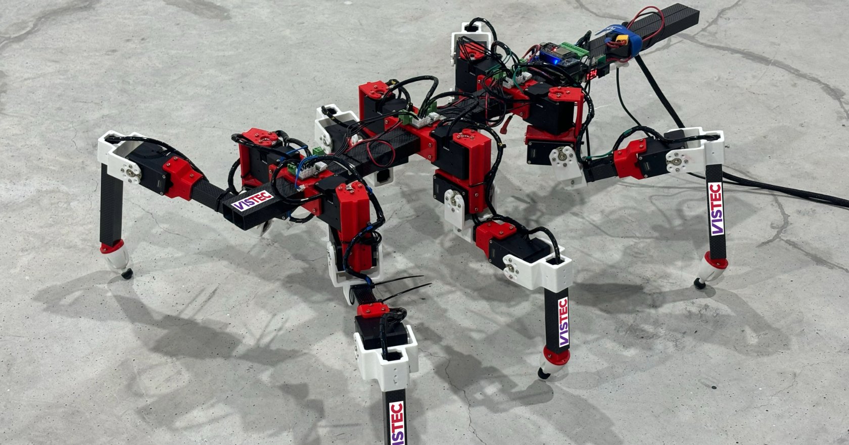 RedMirror six-legged robot with red joint housings and VISTEC labels standing on a concrete floor