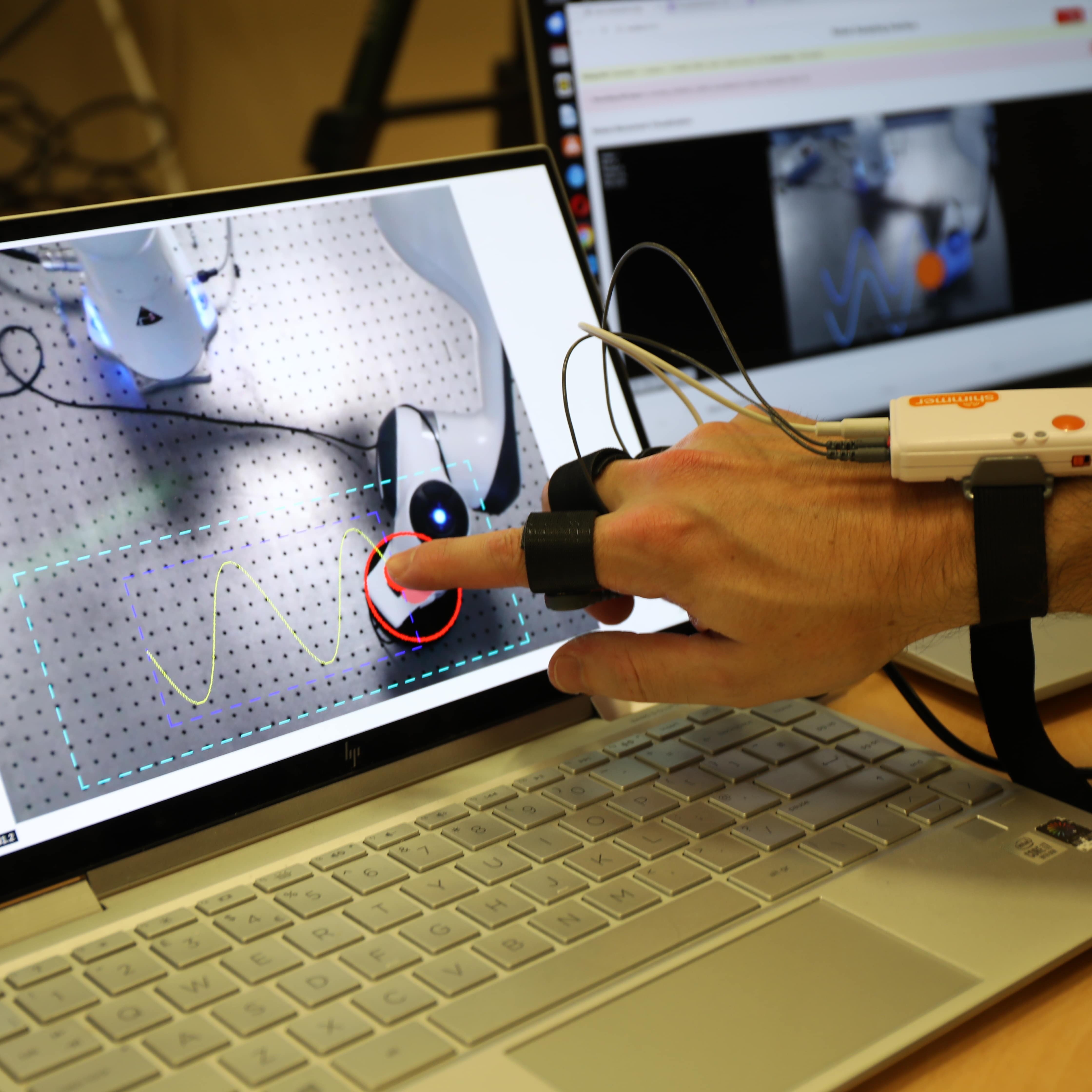 Operator using a touchscreen laptop to guide a Franka arm along a sinusoidal path with finger sensor
