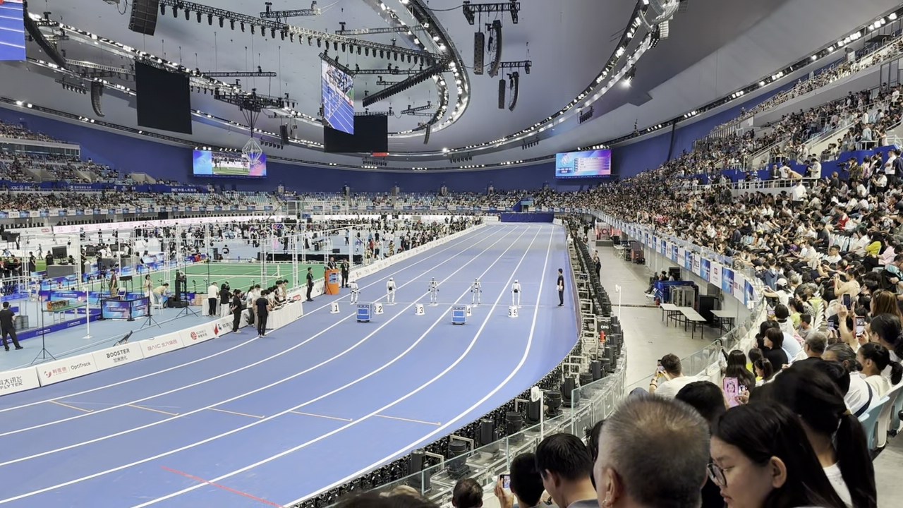 Interior of Beijing’s National Speed Skating Oval during the Games, with a running track in the foreground and a green soccer pitch on the infield