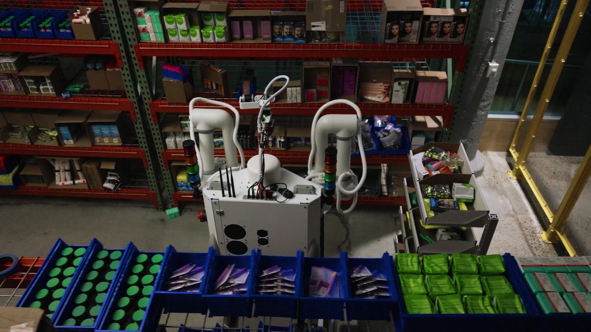 Overhead view of dual-arm Sonny between warehouse shelves and blue totes