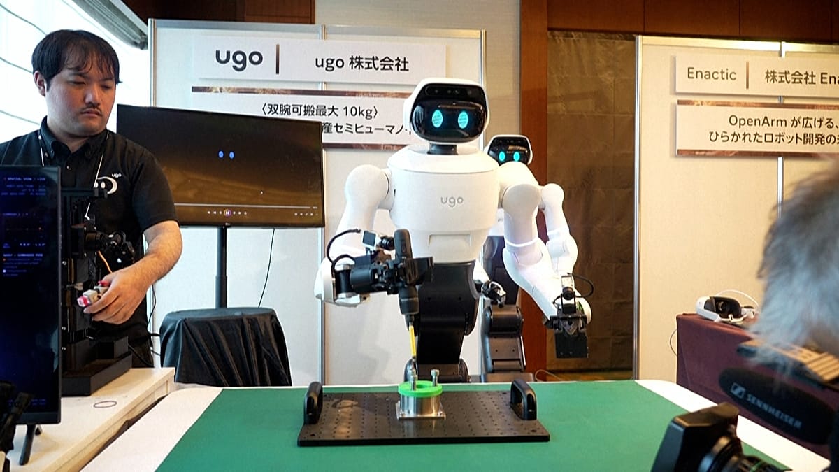 White ugo Nova semi-humanoid drilling a green fixture on a bench while an operator holds a controller