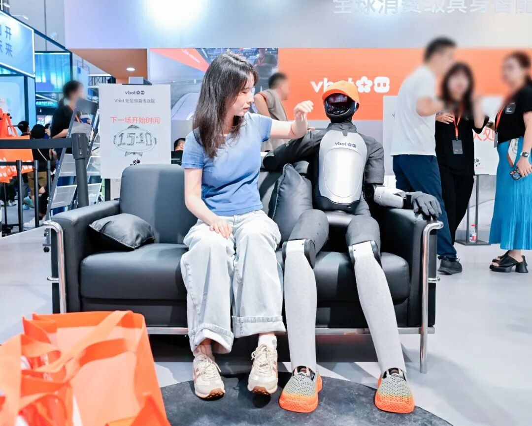 ATOM sitting on a couch in fabric clothing with a face screen and knit shoes