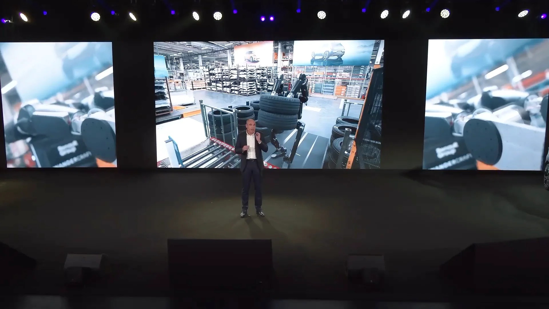 Stage presentation with Calvin-40 carrying stacked tires in a factory still on the screen