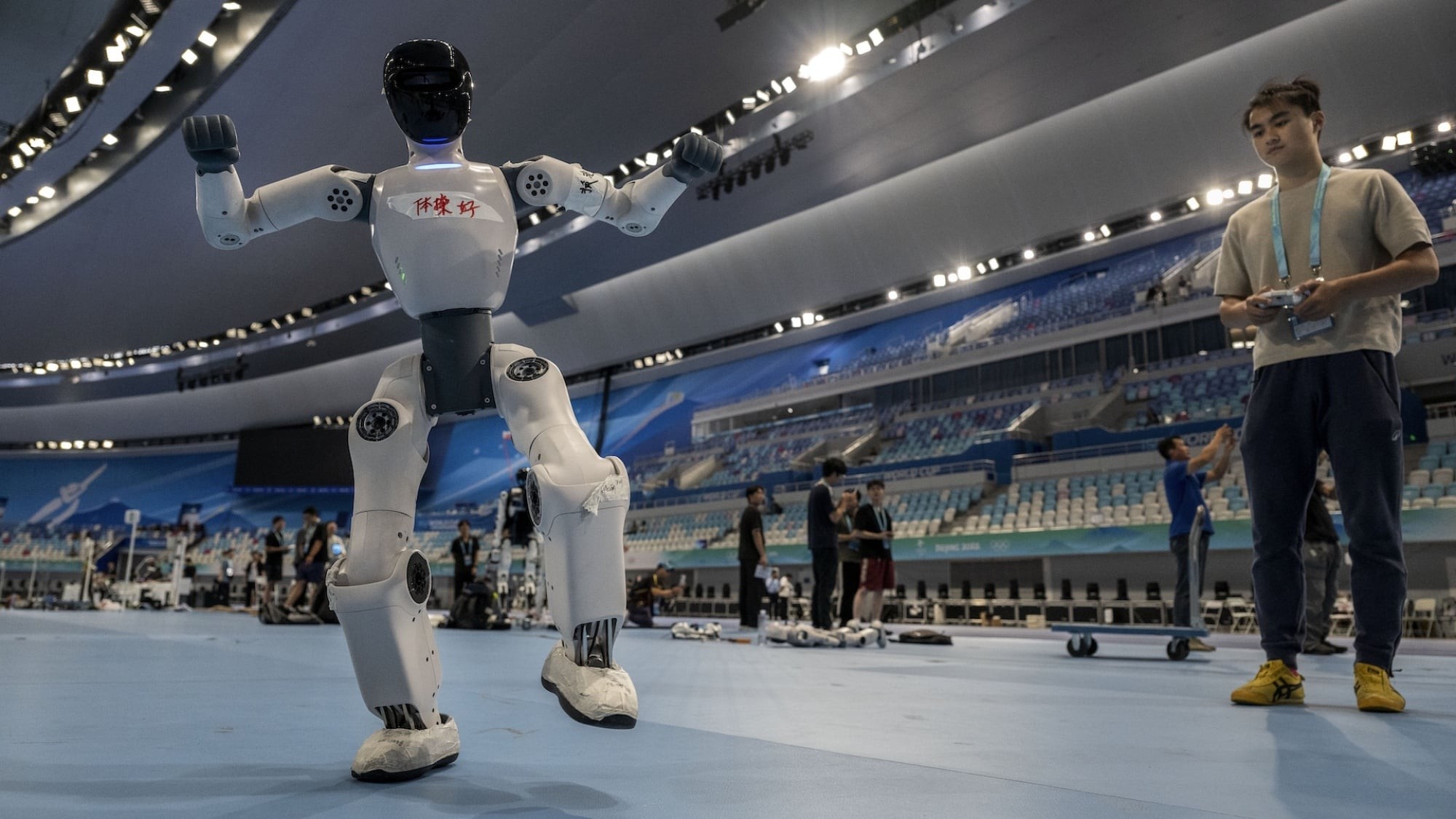 White humanoid practicing a dance pose in the arena with an operator nearby