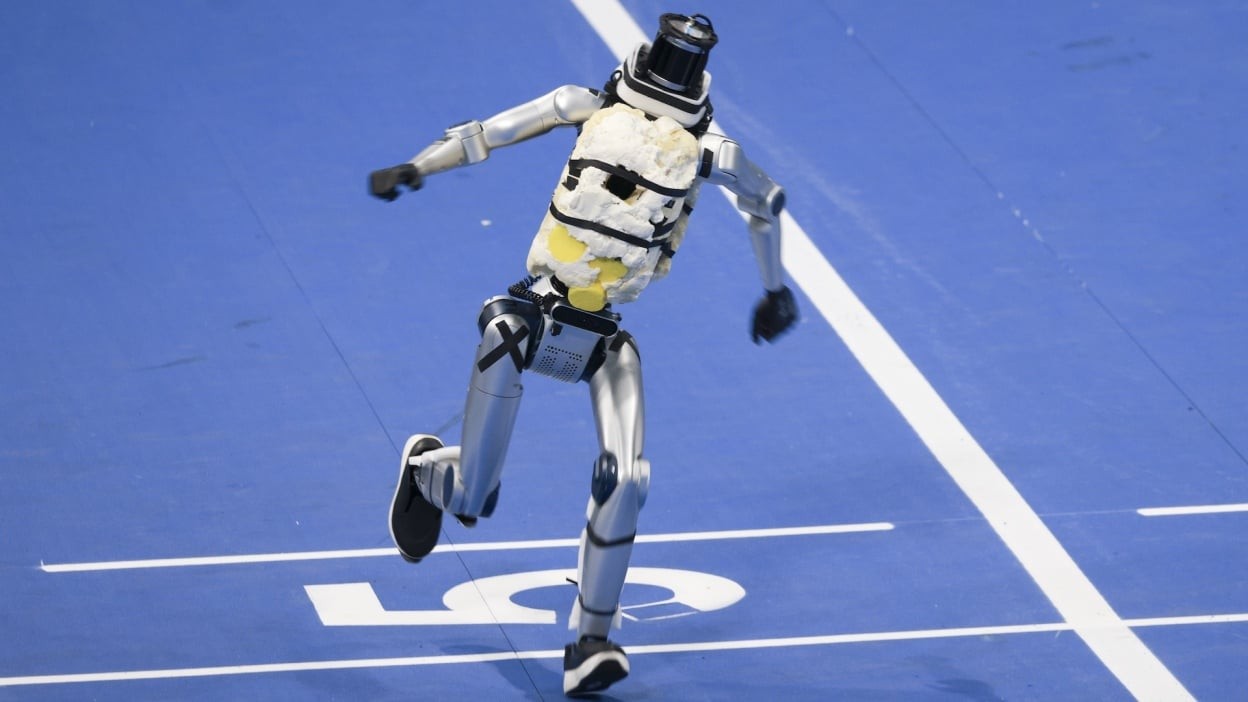Humanoid with foam padding sprinting on a blue indoor track