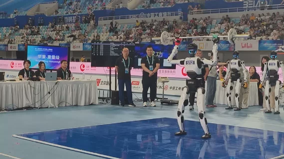 Humanoid robot 512 holding a barbell overhead on a blue platform at the World Humanoid Robot Games