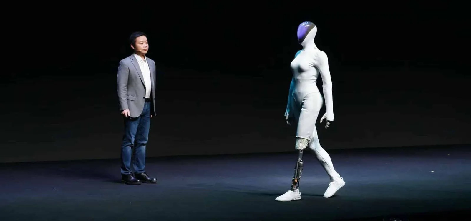 XPeng CEO He Xiaopeng on stage beside the IRON humanoid walking with a cutaway leg