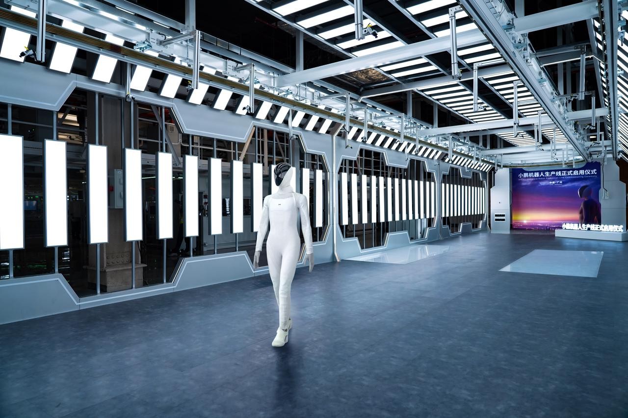 IRON walking down a lit factory corridor at the production-line commissioning ceremony